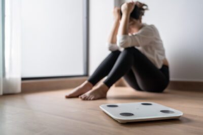 Distressed woman sits on the ground with a scale in front of her.